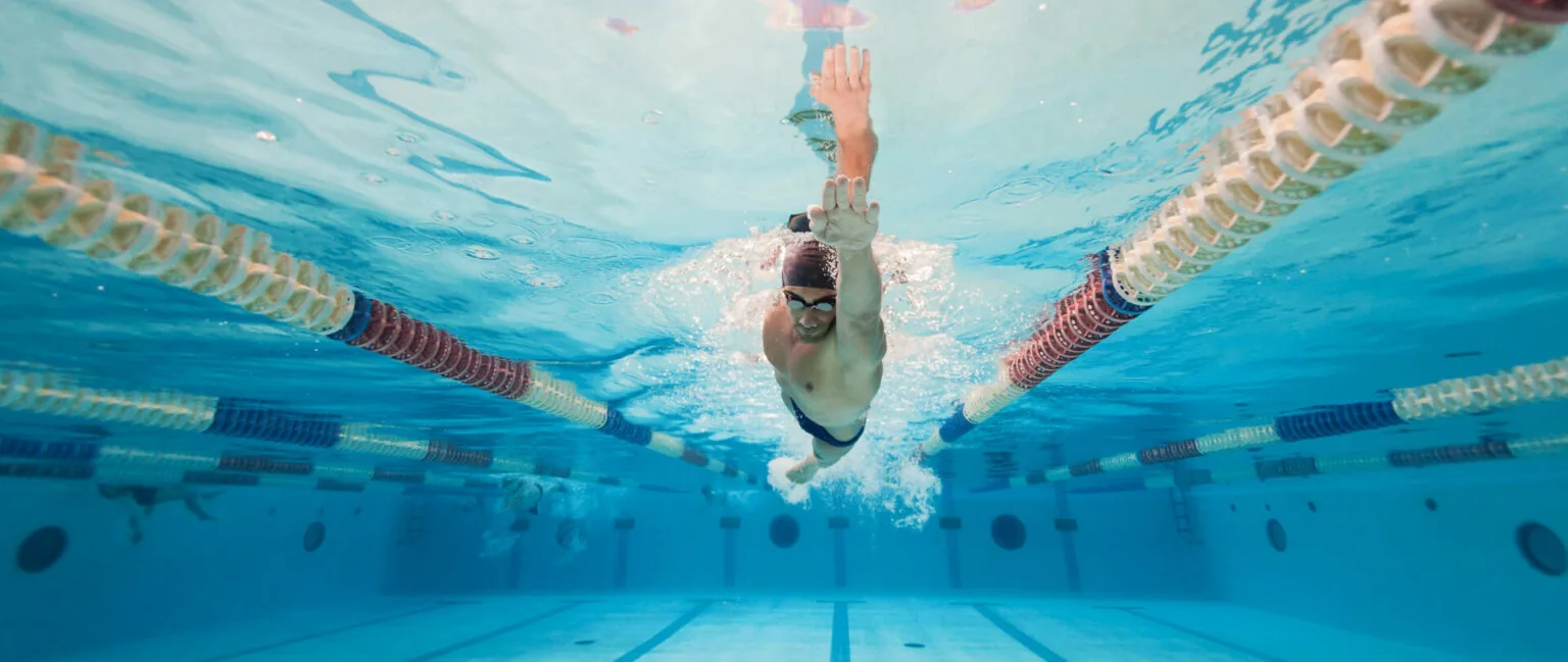 Swimmer performing butterfly stroke underwater in pool with lane dividers on either side