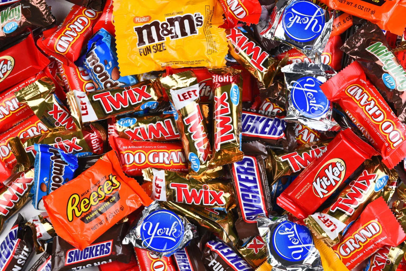 Assorted Halloween candy wrappers including M&Ms, Twix, Snickers, KitKat, Reese's, and other chocolate and peanut candy brands