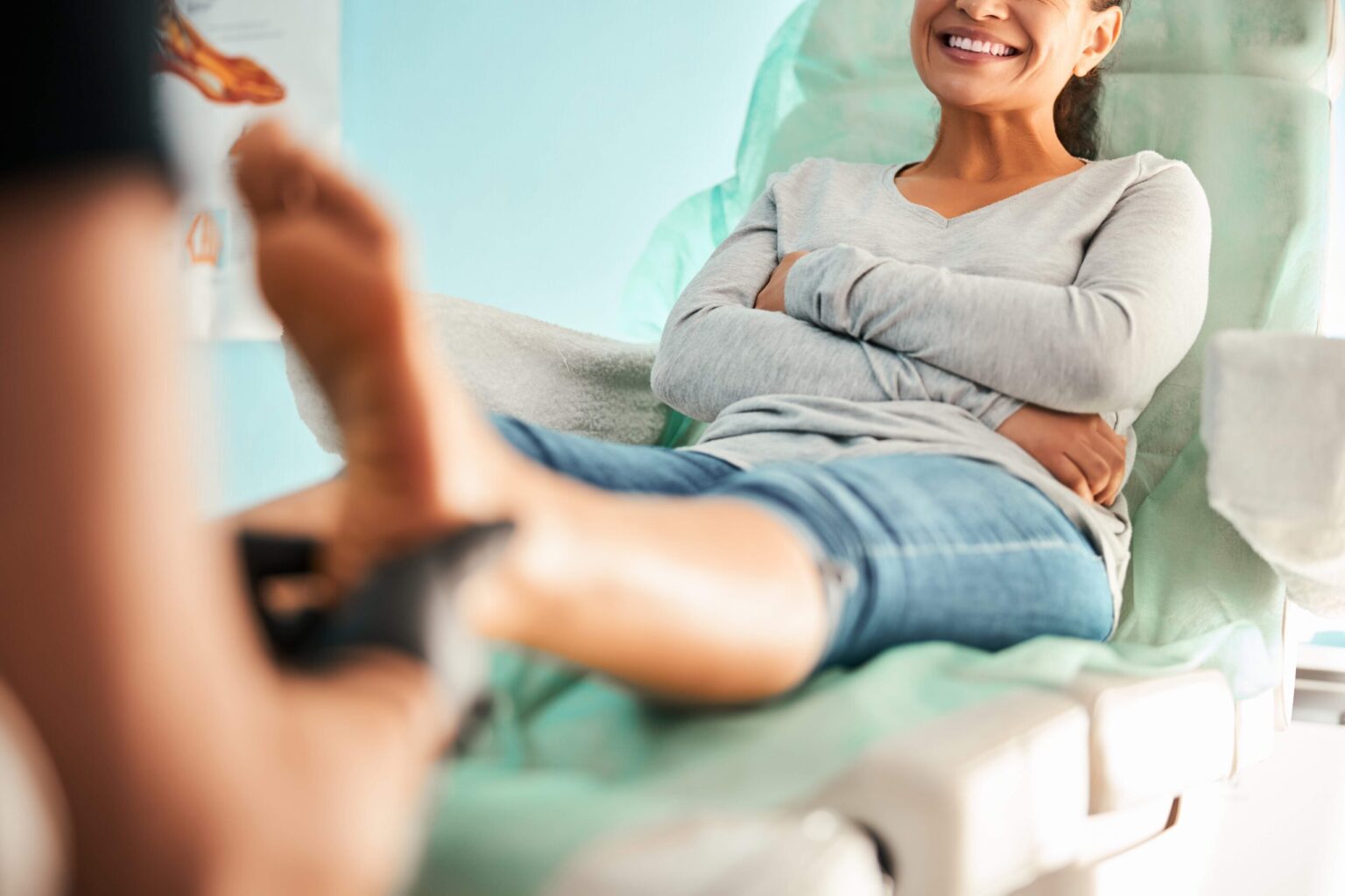 Woman sitting on examination table with feet extended, smiling at healthcare provider during chiropractic consultation