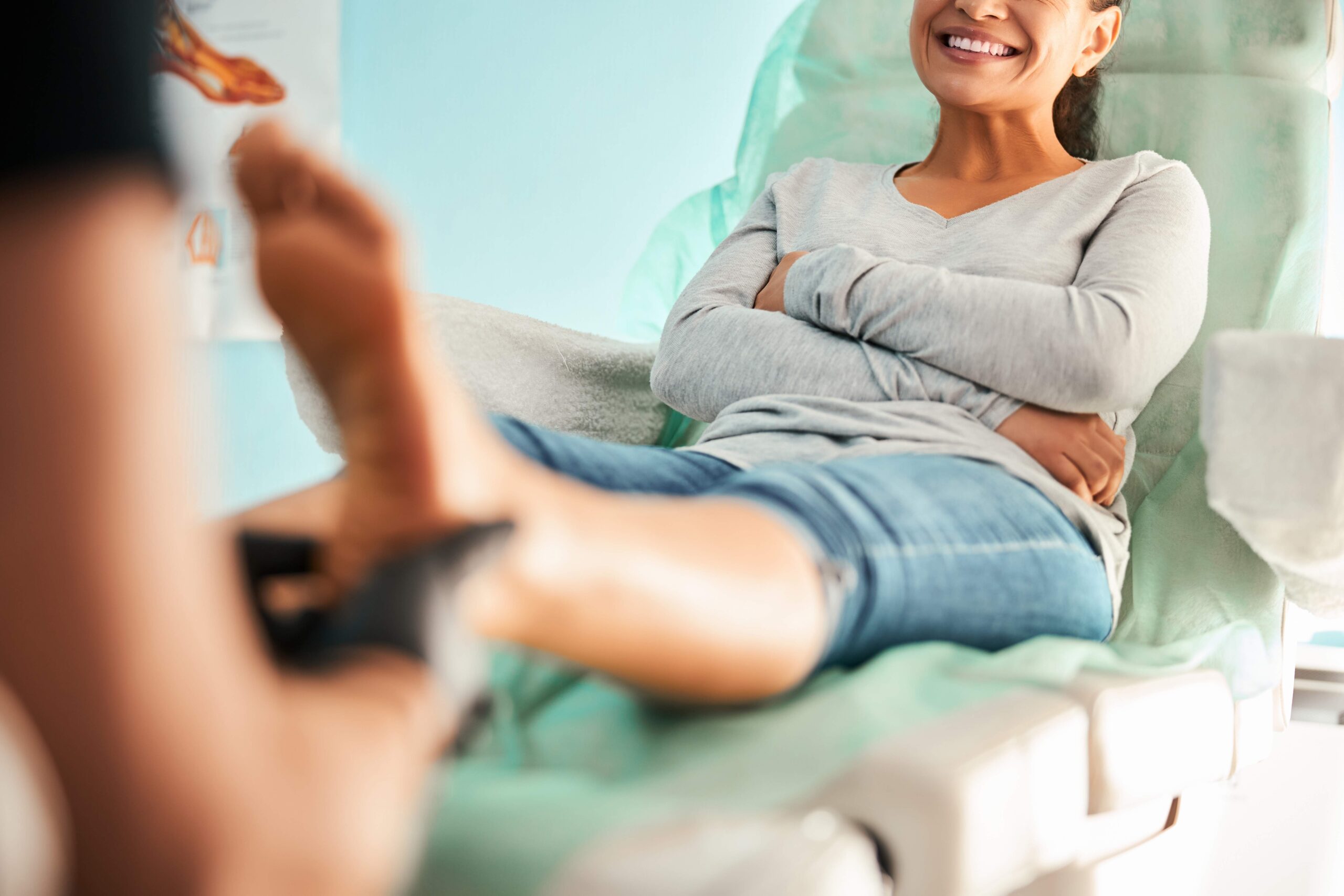 Woman sitting on examination table with feet extended, smiling at healthcare provider during chiropractic consultation