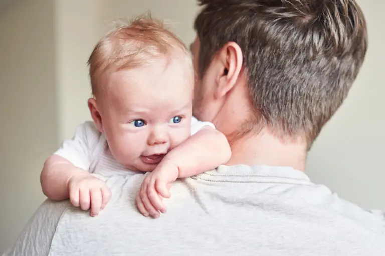 A wide-eyed baby peeks over a parent's shoulder